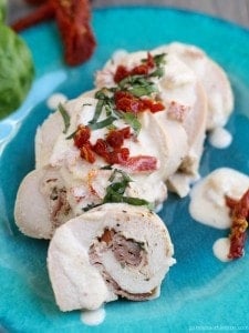 Prosciutto and Pesto stuffed chicken with Sun-dried Tomato and Basil Cream Sauce  on a blue plate with tomatoes.