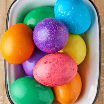 Colored hard boiled eggs in white bowl.
