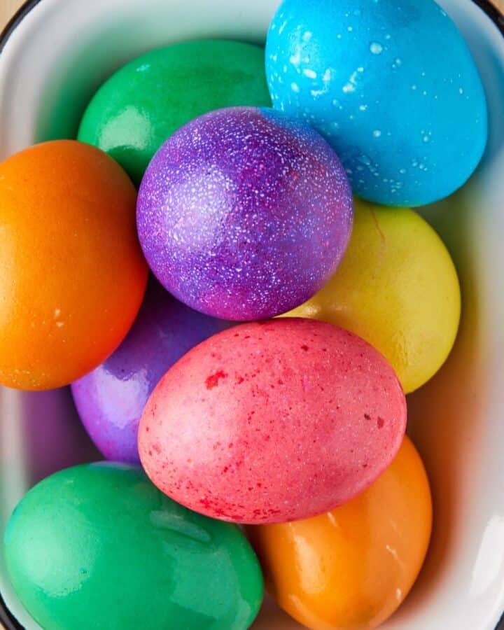 Colored hard boiled eggs in white bowl.