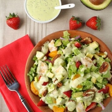 plate of salad with dressing and strawberries on side.
