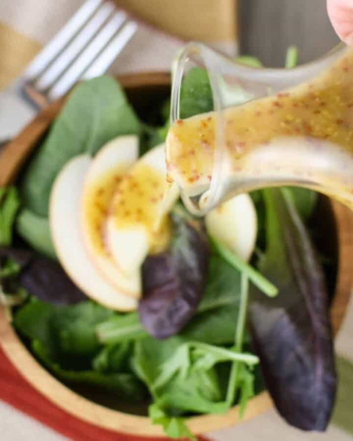 Dijon Vinaigrette in a jar being poured over spinach salad in a wooden bowl.