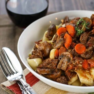 Beef Provencal in a white bowl on top of cream, red, and yellow linens. Fork and knife on side.