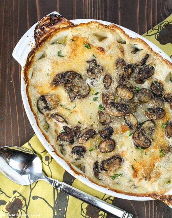 white gratin dish filled with a  provolone, mushroom and potato gratin recipe. It is on a dark brown background.