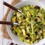 Shaved brussel sprouts salad in a white bowl on top of brown linens and a white backdrop.