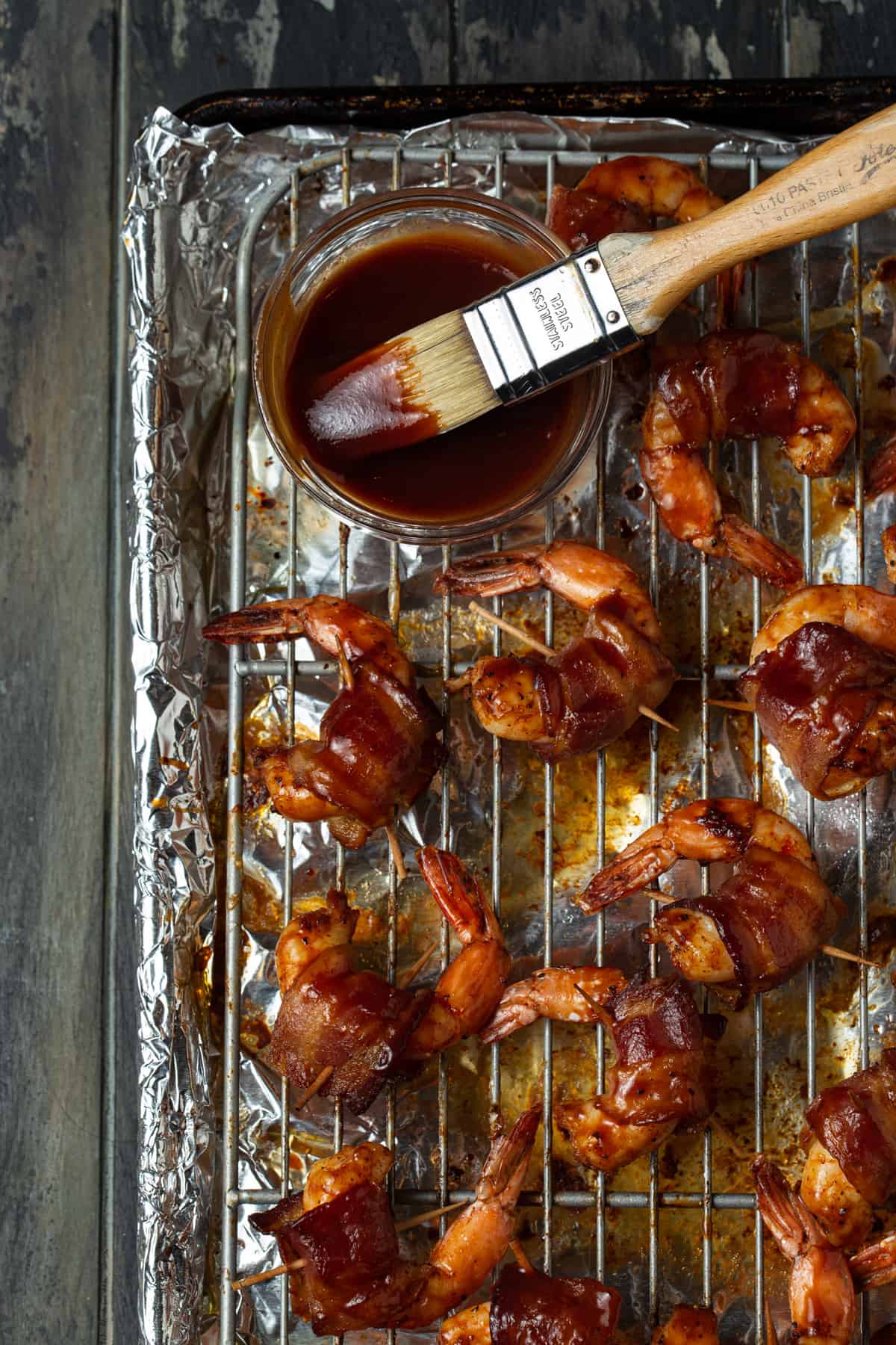 shrimp on a baking sheet with barbecue sauce and brush.