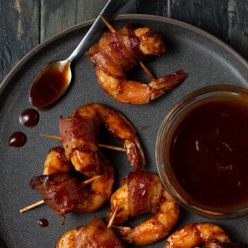 A plate of bacon wrapped shrimp with barbecue sauce.