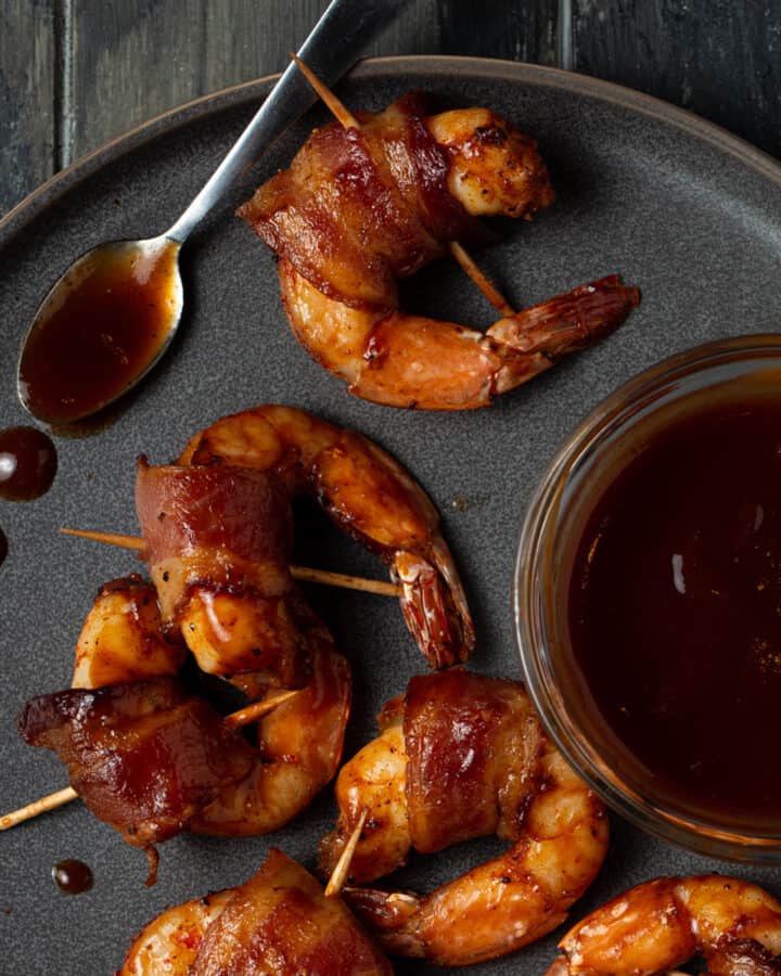 A plate of bacon wrapped shrimp with barbecue sauce.