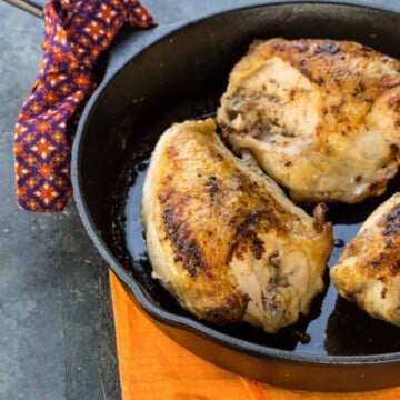 Three bone-in chicken breasts on a black skillet pan.