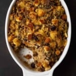 A close up of a bowl of food on a plate, with Cornbread.