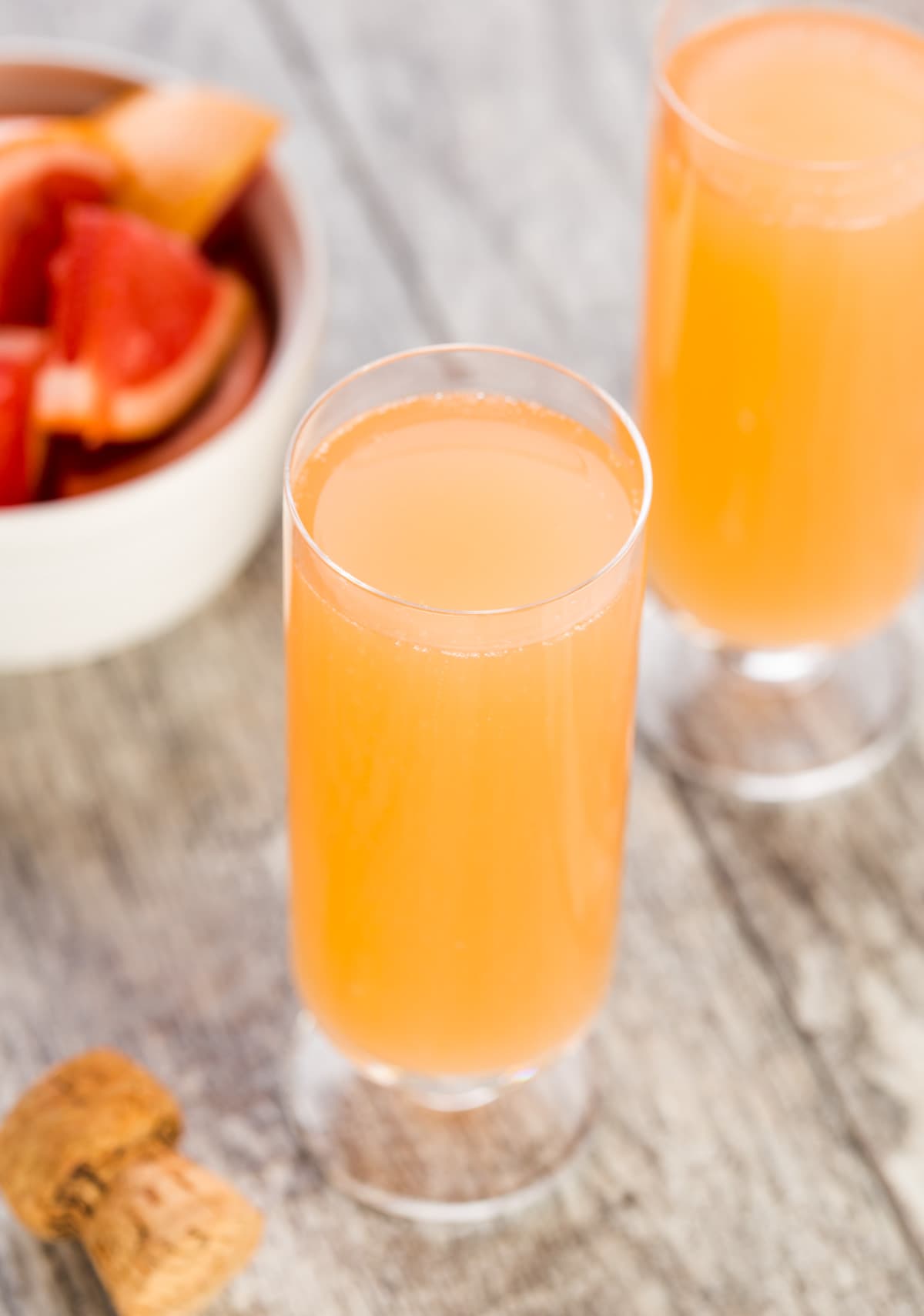 two champagne flutes filled with mimosas and a bowl of fresh grapefruit in a bowl for garnish.