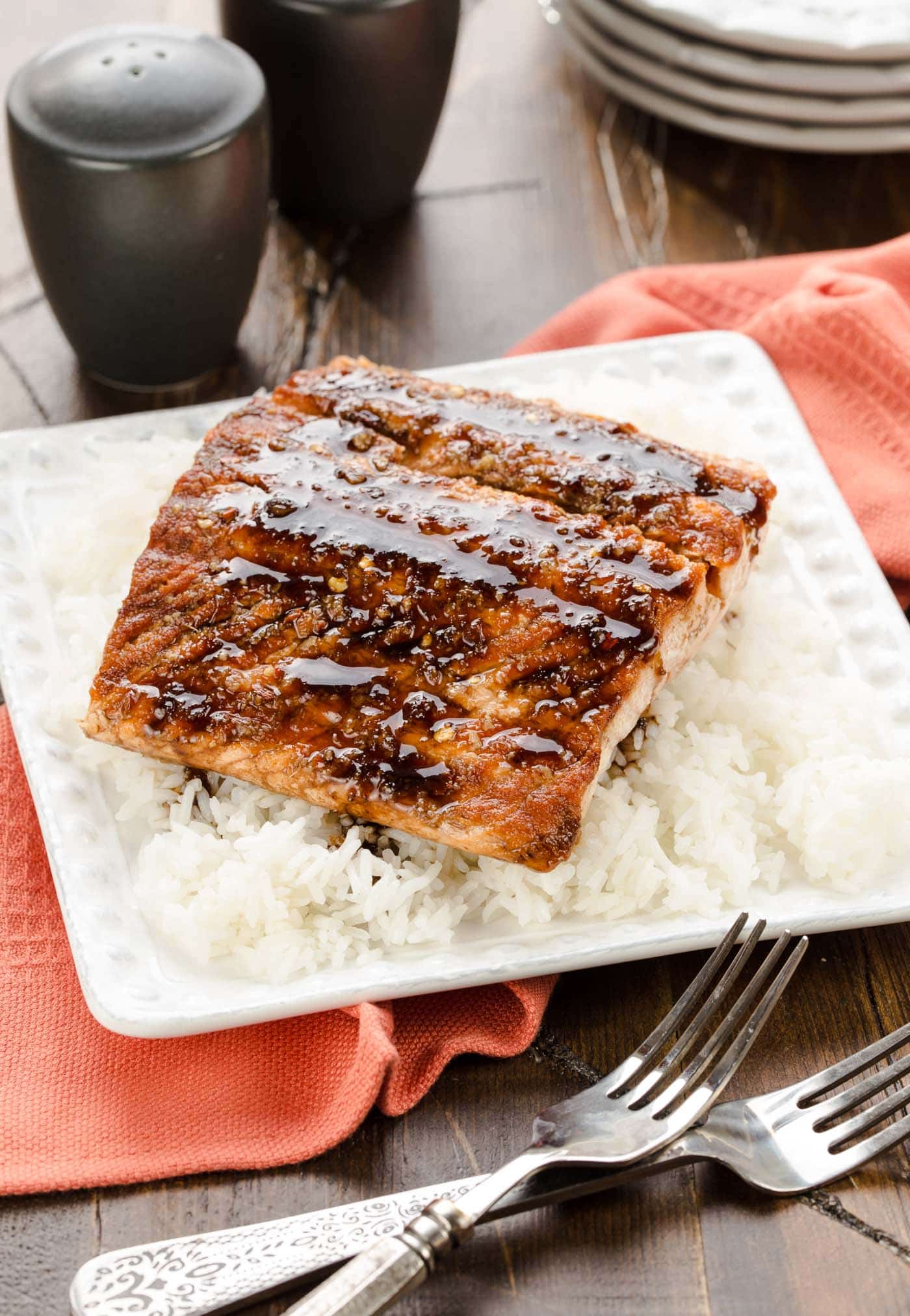 Salmon with glaze on rice on white plate.
