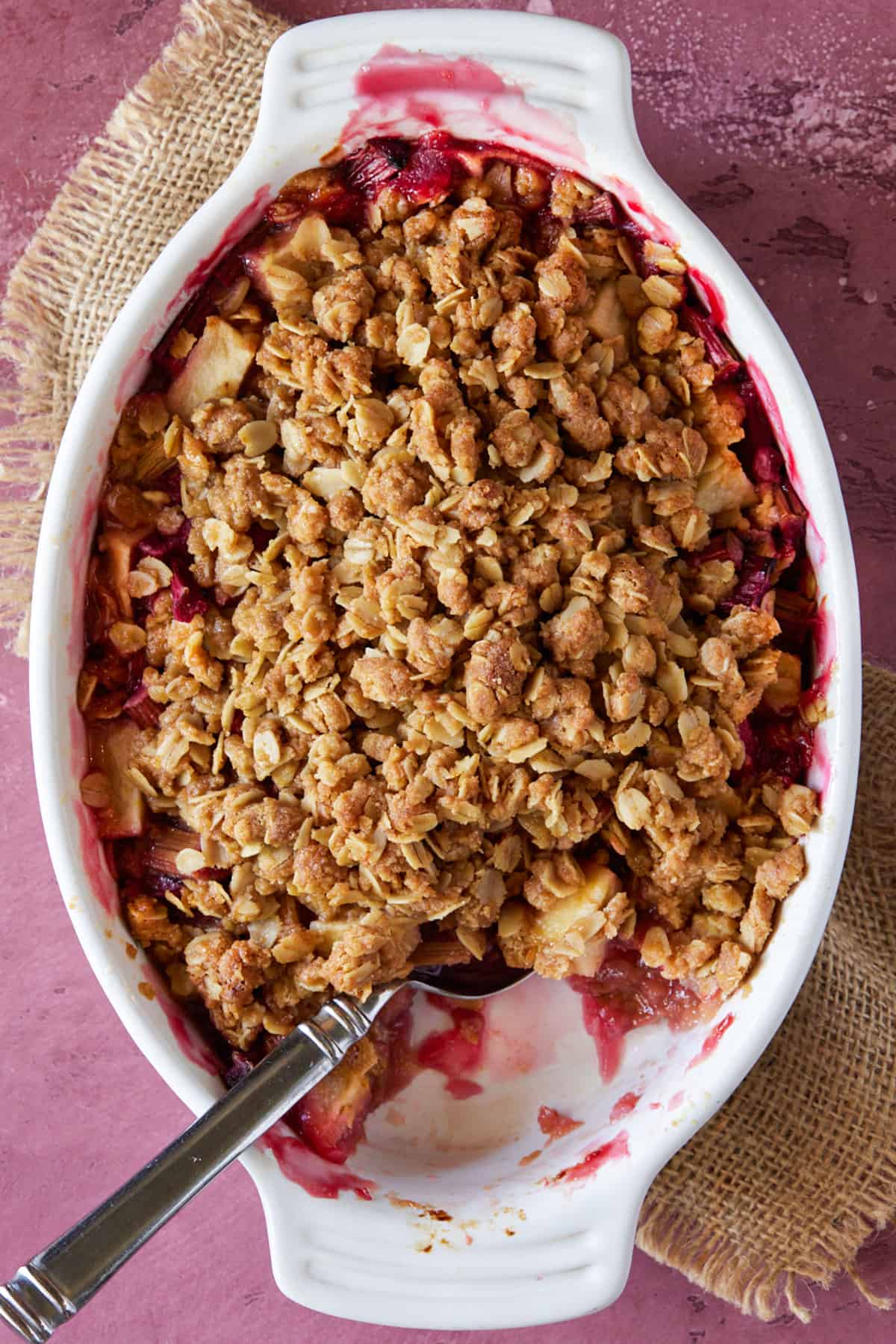 white pan filled with fruit crisp with a scoop out and a spoon for serving.