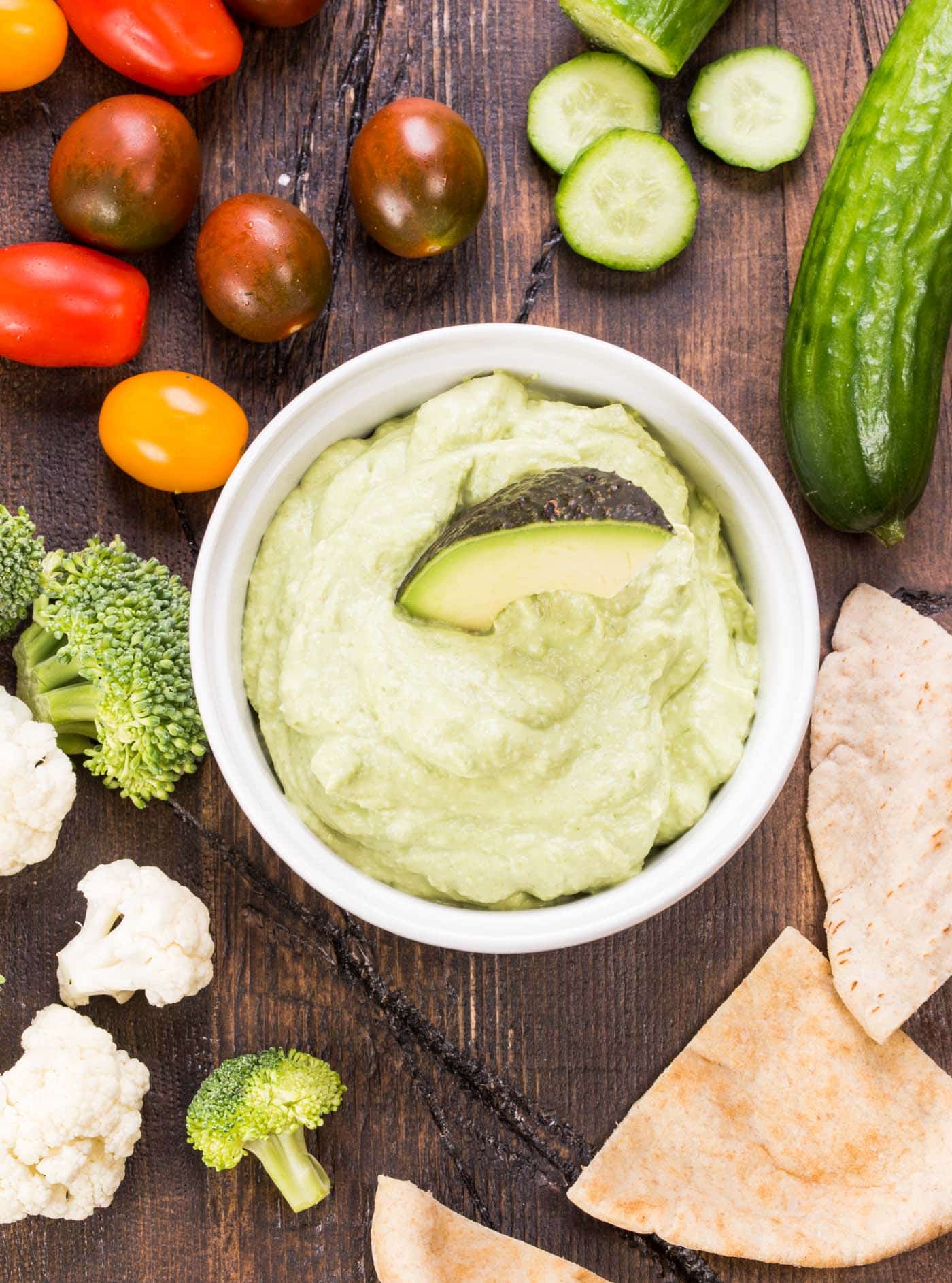 A bunch of dip on a tray, with Avocado and vegetables.