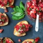 Crostini on dark background with chopped tomatoes and basil.