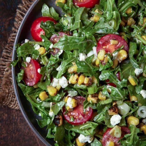 arugula salad on plate with corn and tomatoes.