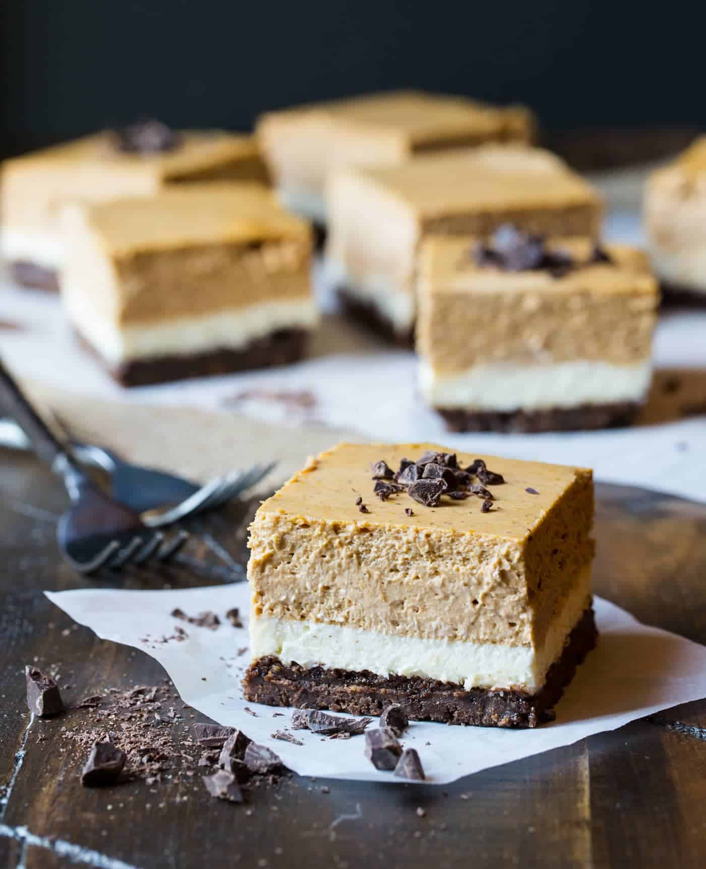 Layered cheesecake bars on parchment.