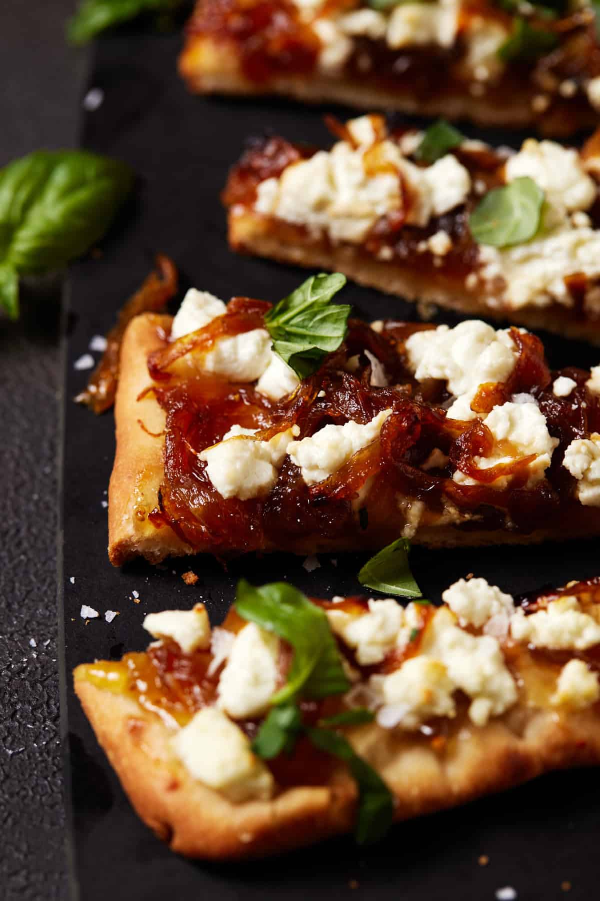 Slices of Goat Cheese pizza with basil on a black cutting board. 