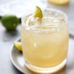 Lime Margarita in low ball glass with lime wedges.