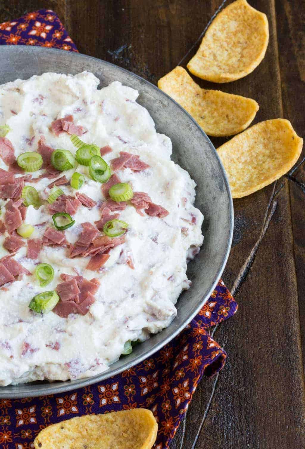 dip in a metal baking dish on a dark background with corn chips for eating.