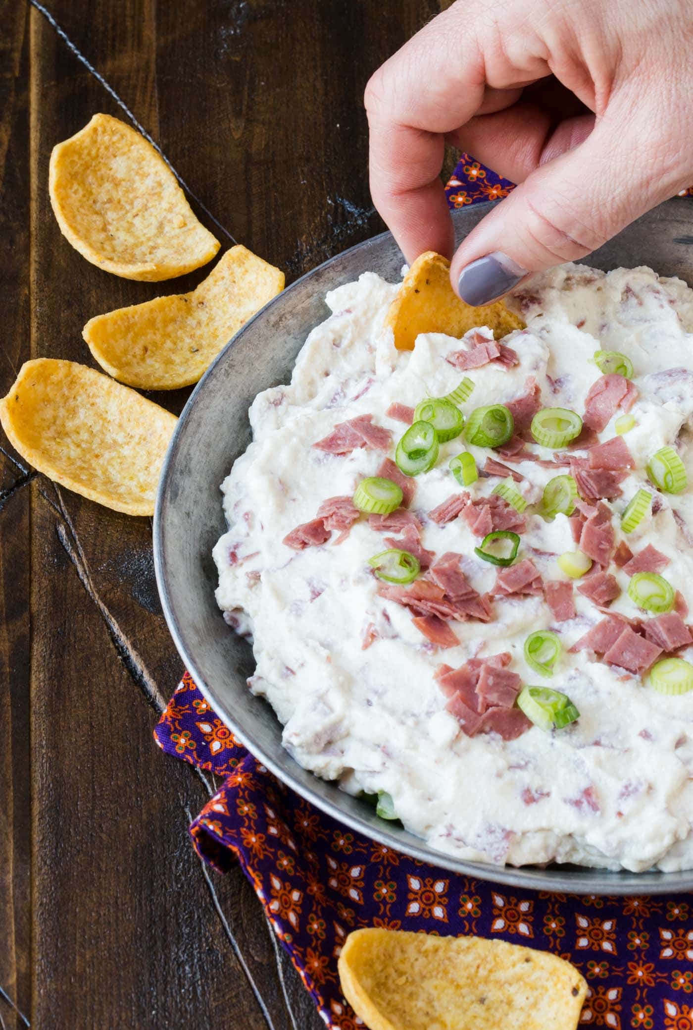 A close up of a person holding a plate of dip with Chipped beef.