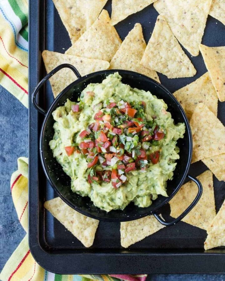 A tray filled with Guacamole, chips and Avocado.