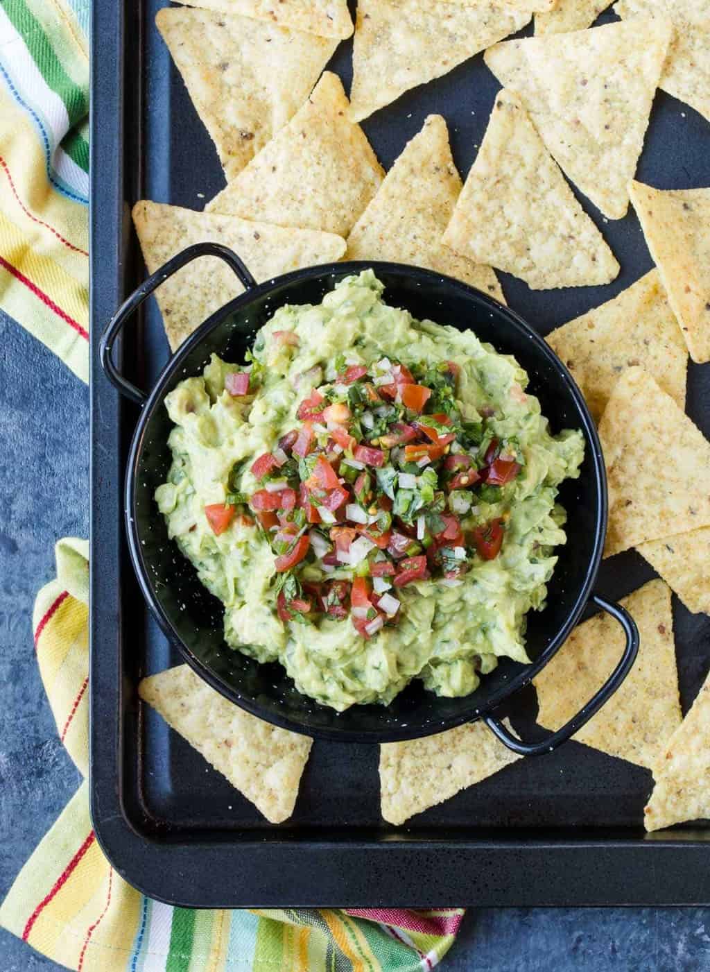 A tray filled with Guacamole, chips and Avocado.