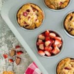 A muffin pan filled with muffins, with strawberry and rhubarb.