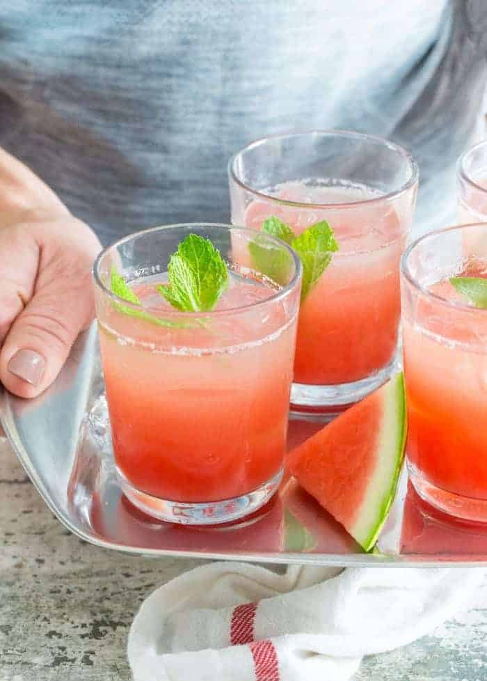 Person holding tray of watermelon gin punch with fresh mint.