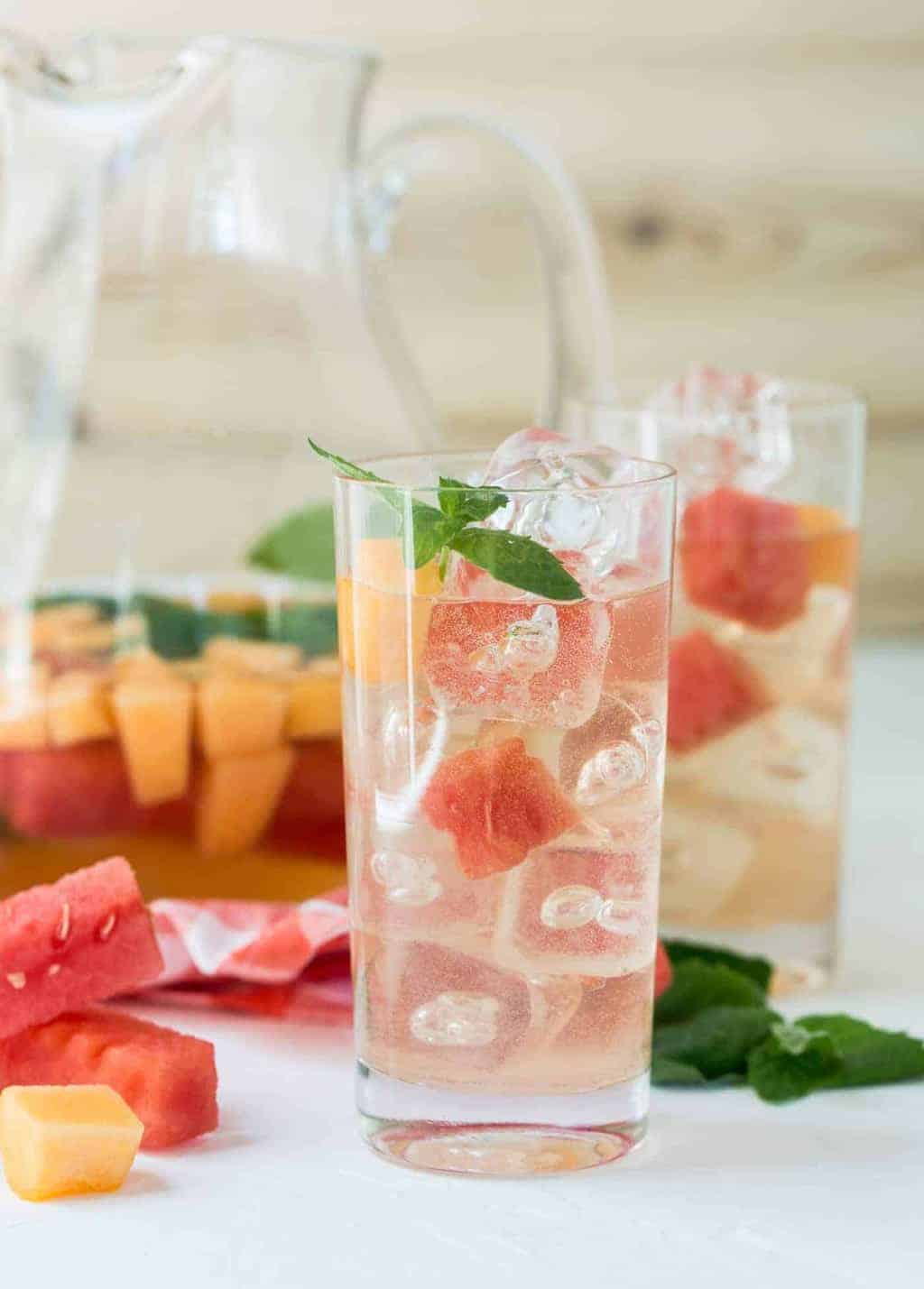 Elderflower Sangria in high ball glass with watermelon and cantaloupe cubes and mint leaves.