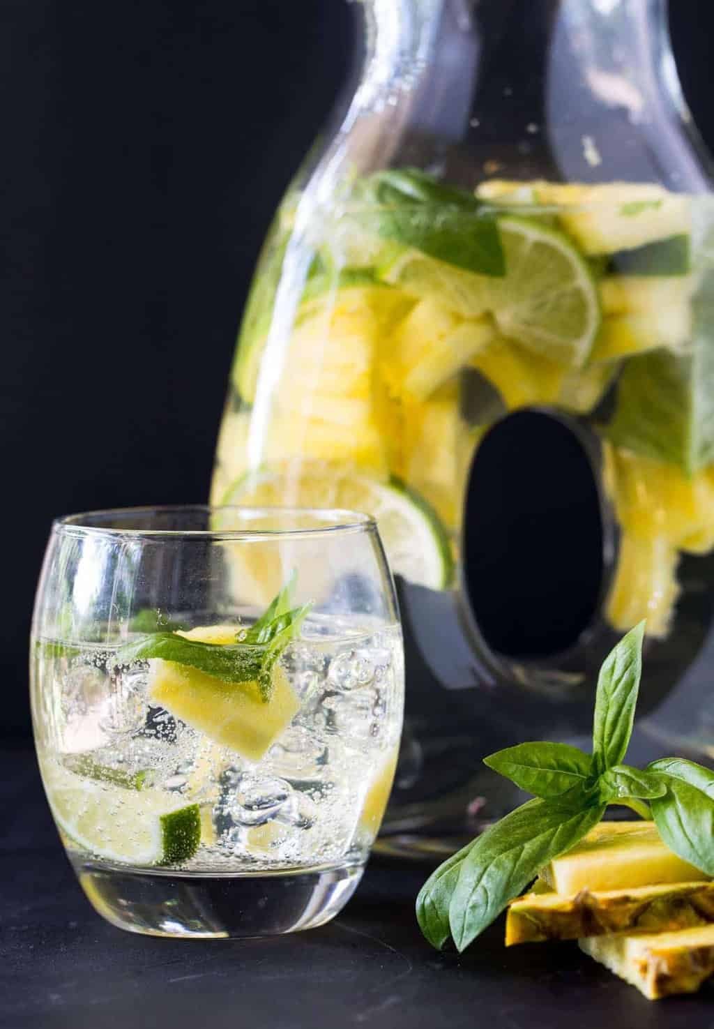 pineapple sangria in glass with pitcher full of sangria pineapple and limes.