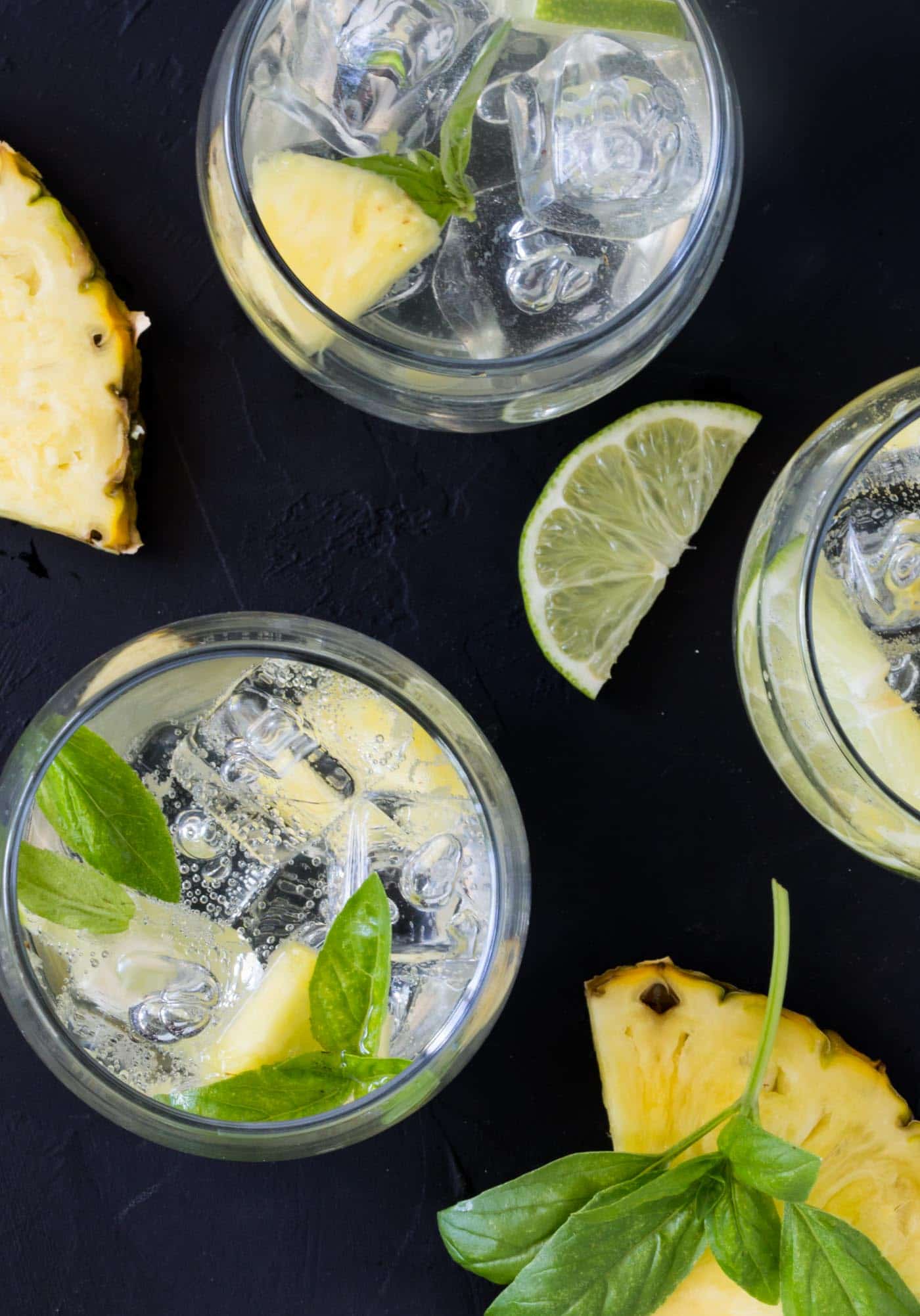 glasses on Pineapple Sangria on a black background with pineapple wedges, lime slices and basil.