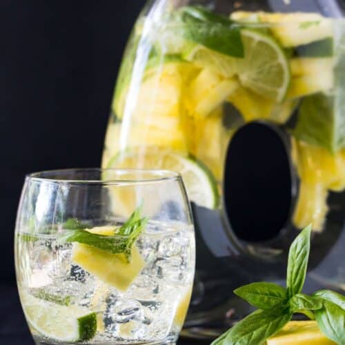pitcher filled with pineapple and mint with glass filled with ice and drink.