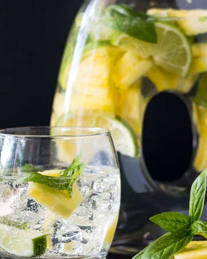 pitcher filled with pineapple and mint with glass filled with ice and drink.