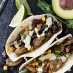 Two Corn and Mushroom Tacos with poblano peppers, avocado crema, salsa verde and avocado and lime slices.