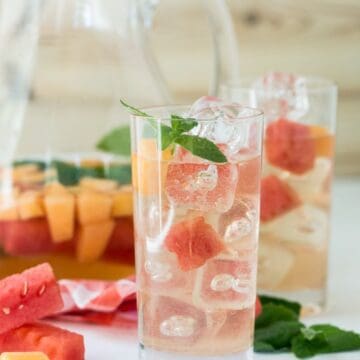 glass filled with drink , ice and melon cubes.