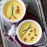 Two bowls of creamy Sweet Corn Soup on a silver tray garnished with crispy pancetta bits and chives.