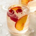 Glass of Rosé Sangria garnished with fresh peach slices and raspberries.