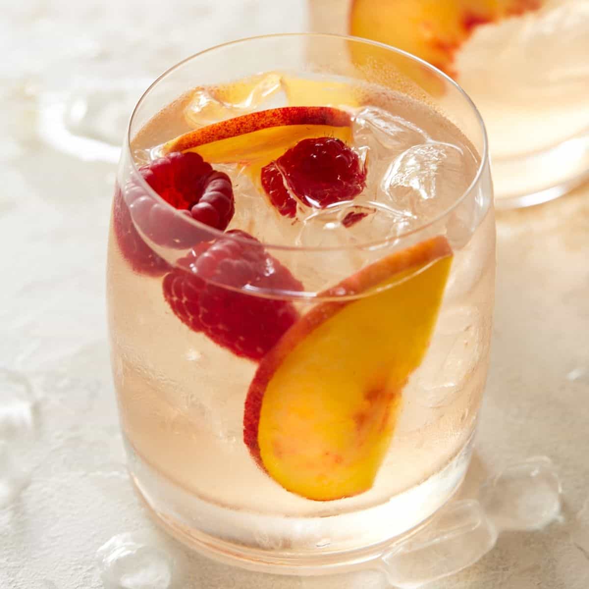 Glass of Rosé Sangria garnished with fresh peach slices and raspberries.