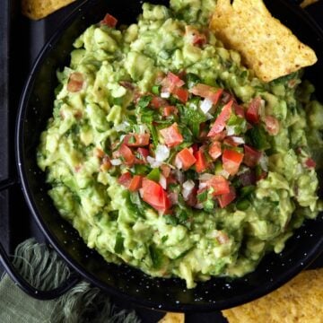 Chunky guacamole in a black metal bowl with tortilla chips.