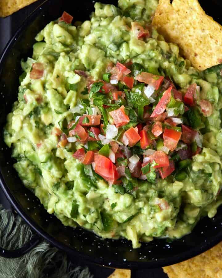 Chunky guacamole in a black metal bowl with tortilla chips.
