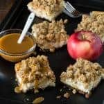 Caramel Apple Cheesecake Bars with Biscoff Cookie Crust on a dark sheet pan, with caramel and apples.