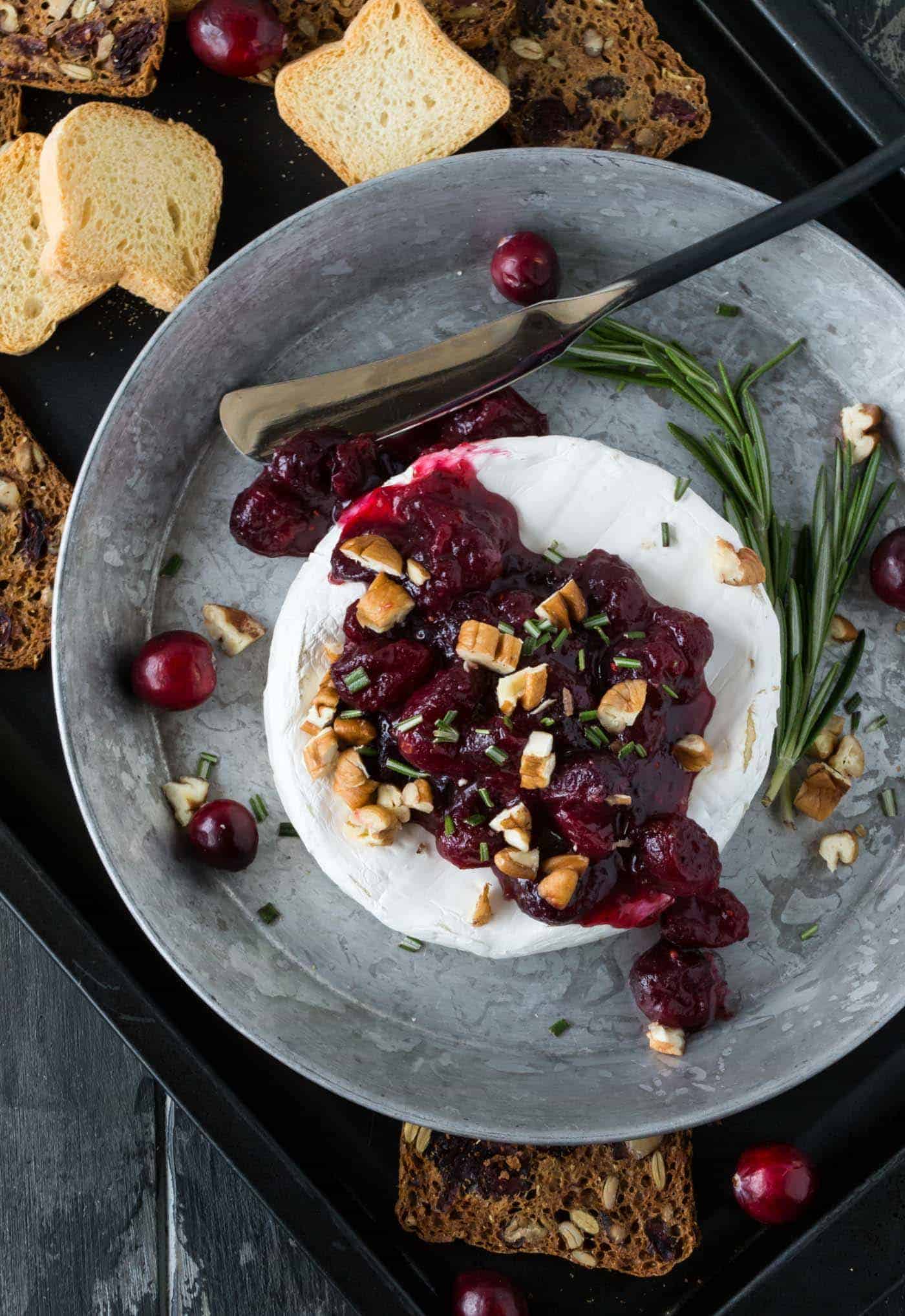 Brie topped with cranberry compote in a silver tray with crackers.