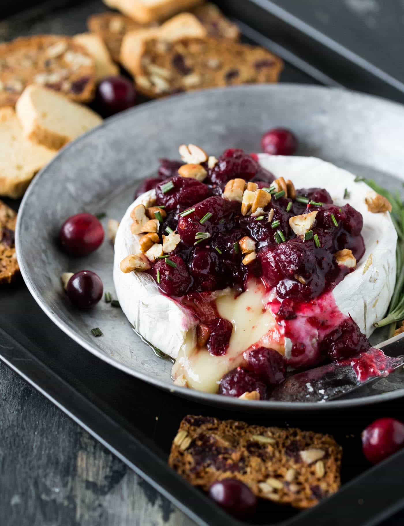 Warm brie topped with cranberries and pecans surrounded by crackers and mini toasts.