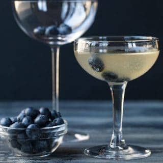 Blueberry Martini is a coupe glass with blueberry floating in it for garnish.