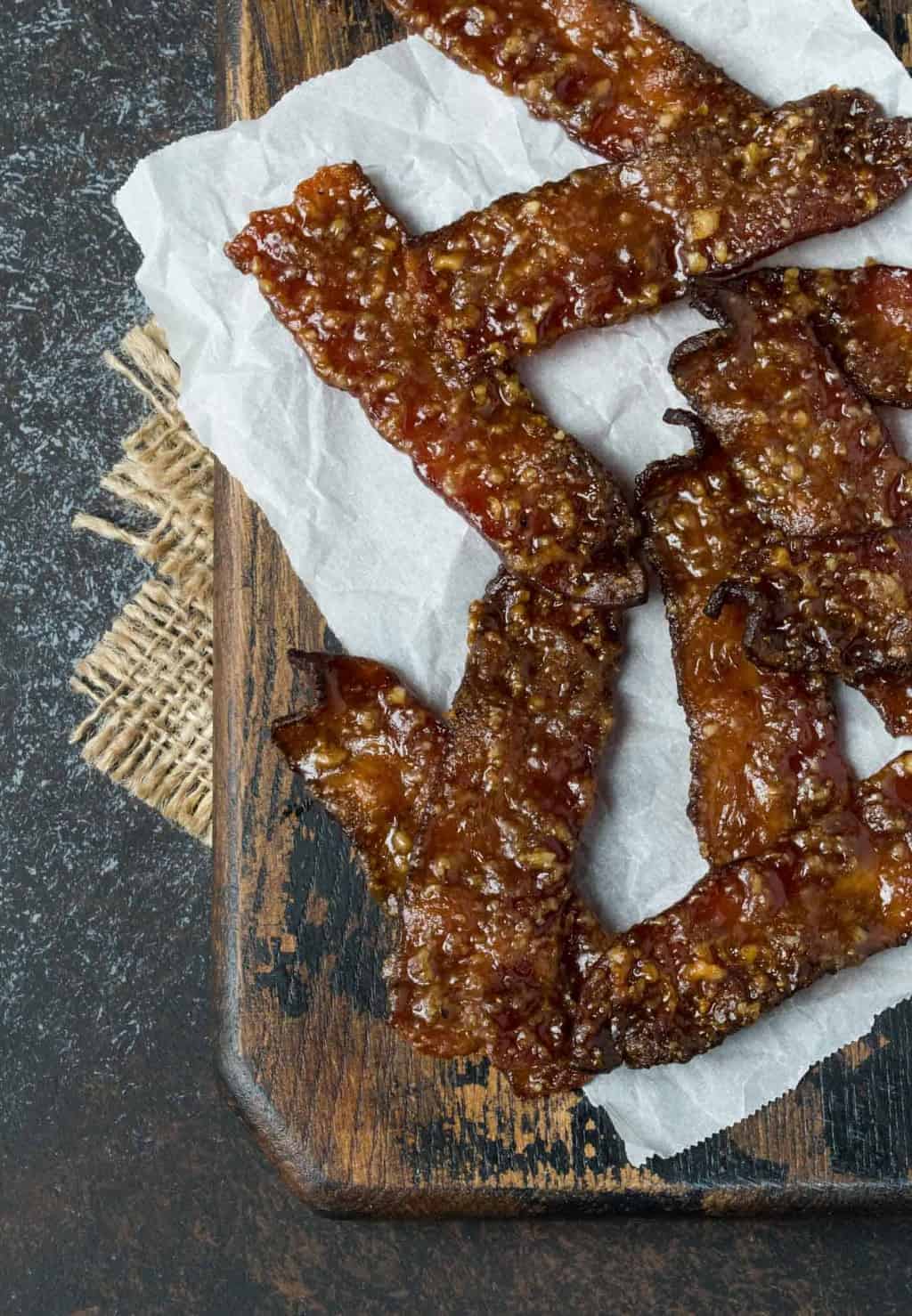 Candied Bacon piled on a wodden serving tray with parchment paper.