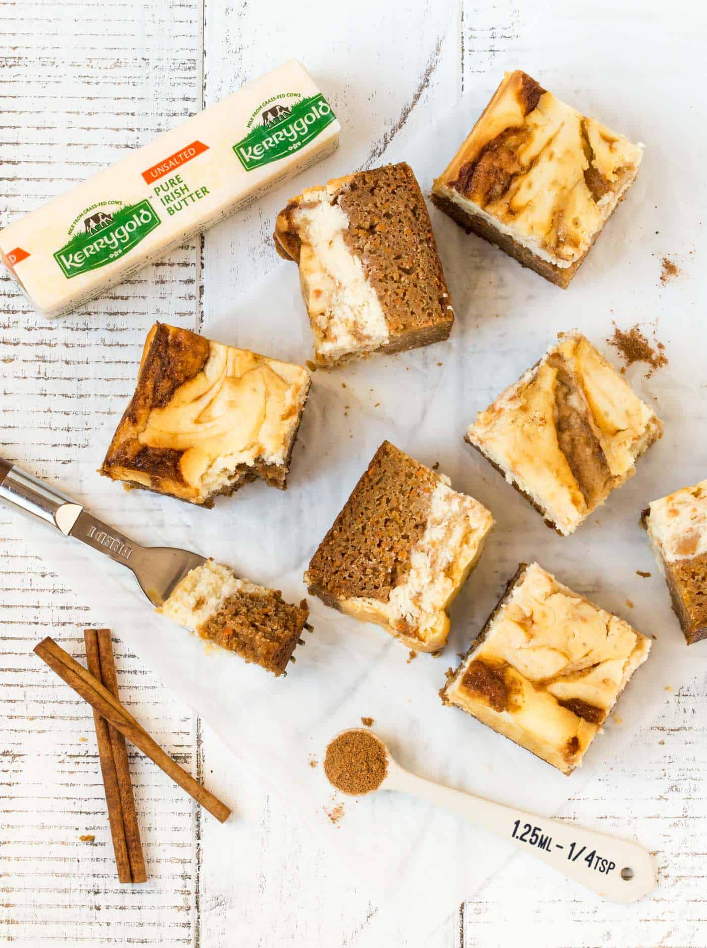  cut carrot cake cheesecake bars on white background with fresh cinnamon sticks for garnish.