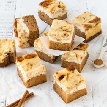 Carrot Cake Cheesecake Bars cut into squares on white surface with ground cinnamon for garnish.