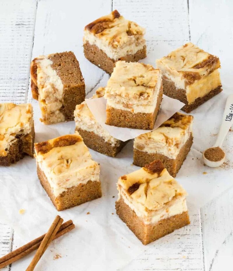 Carrot Cake Cheesecake Bars cut into squares on white surface with ground cinnamon for garnish.