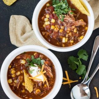 two bowls of slow cooker chicken taco soup garnished with fresh cilantro, sour cream and chips.