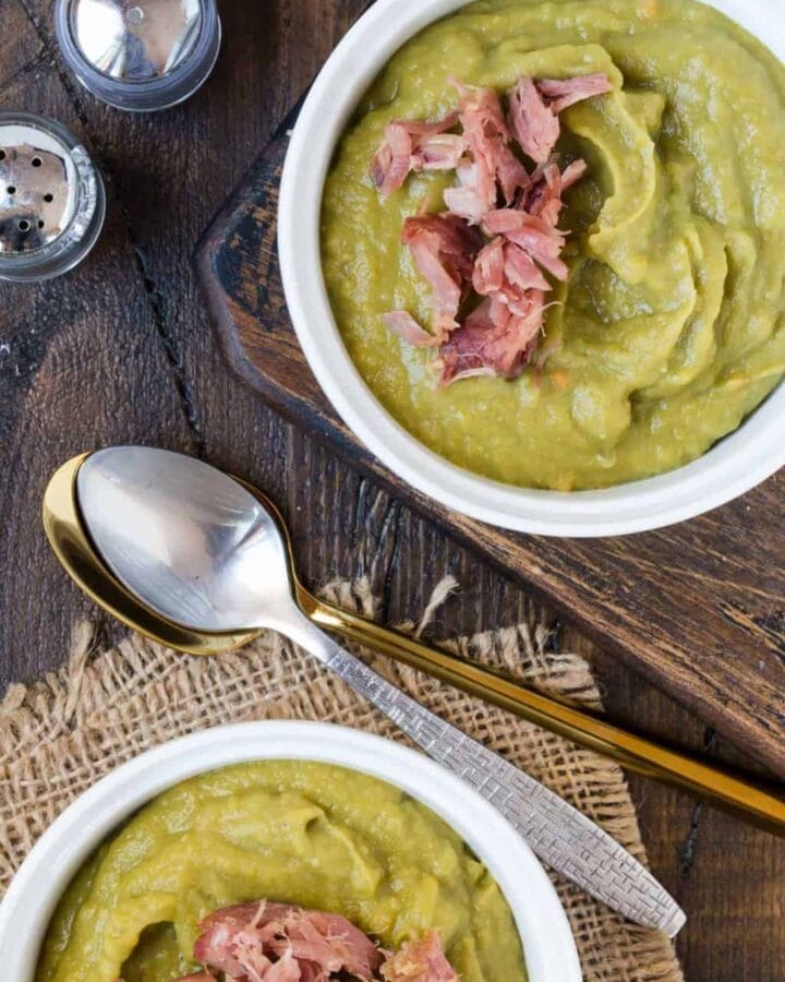 Two bowls of Slow Cooker Split Pea Soup with Ham and two spoons, with shredded ham.